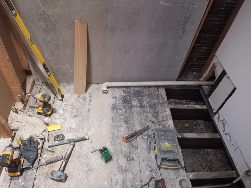 Bathroom mid strip-out, subfloor exposed with tools and a spirit level on the floor.