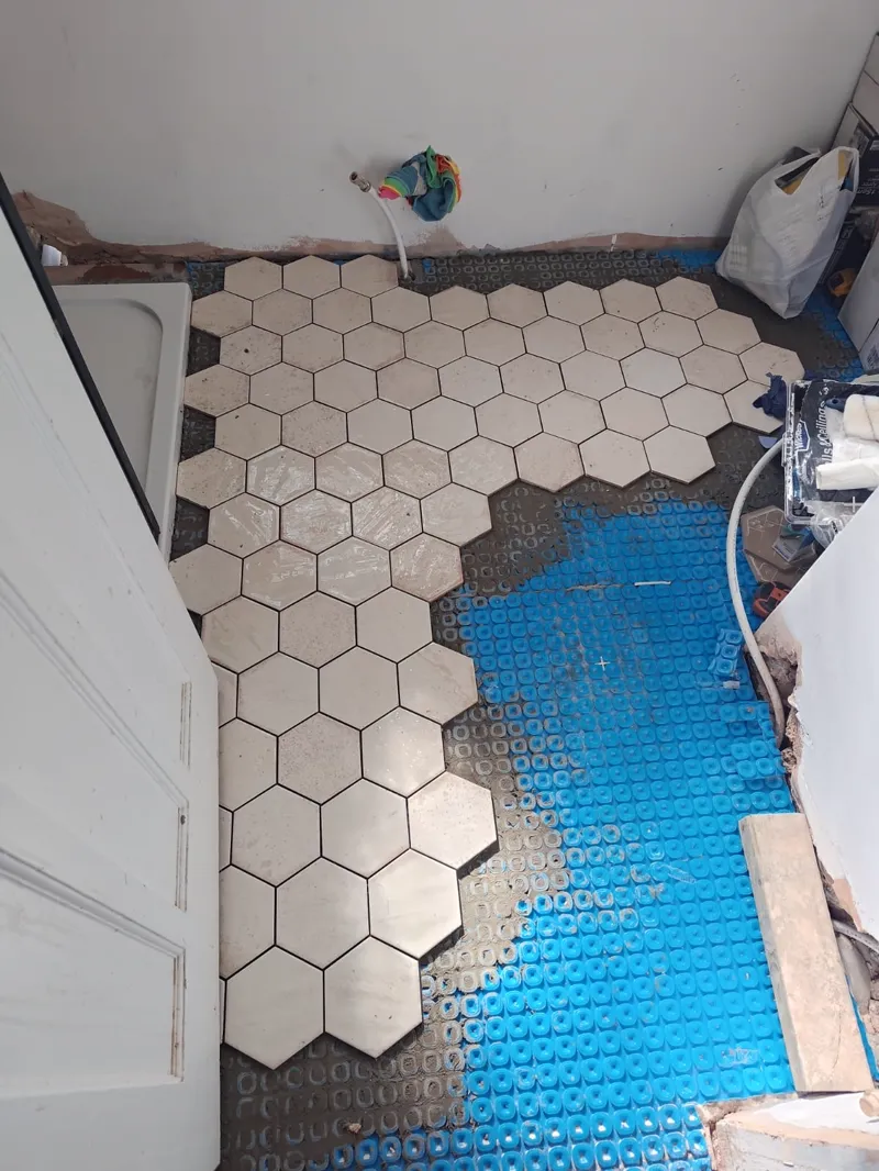 Hexagonal floor tiles being laid over a blue underfloor-heating mat, spacers in place.