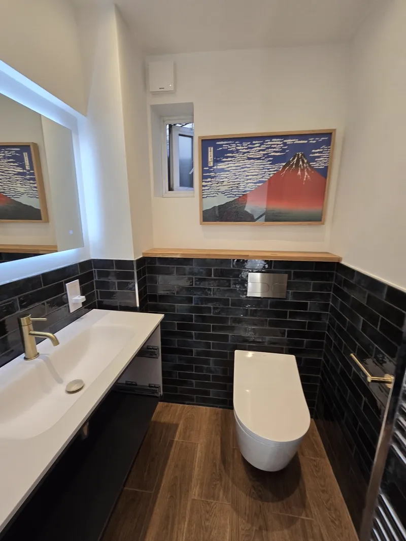 Completed cloakroom with black metro-tile walls, a wall-hung toilet and wood-look flooring.