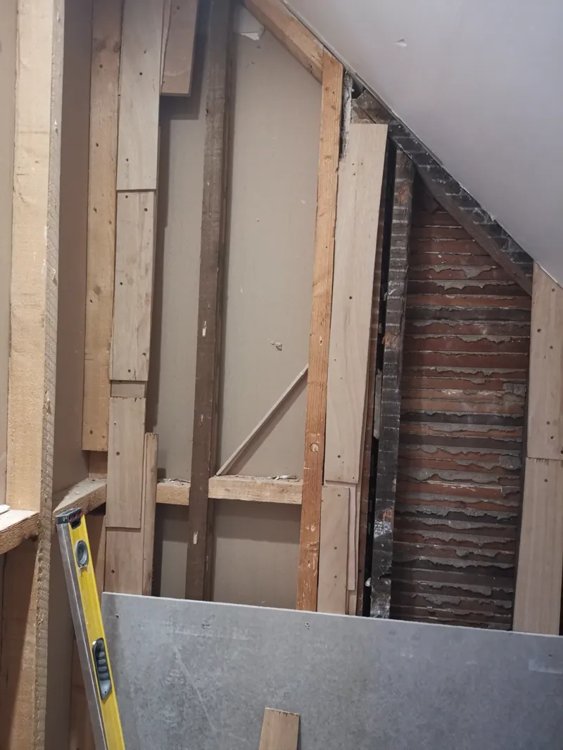 Timber stud wall built into a loft eaves space with exposed brick chimney breast alongside.