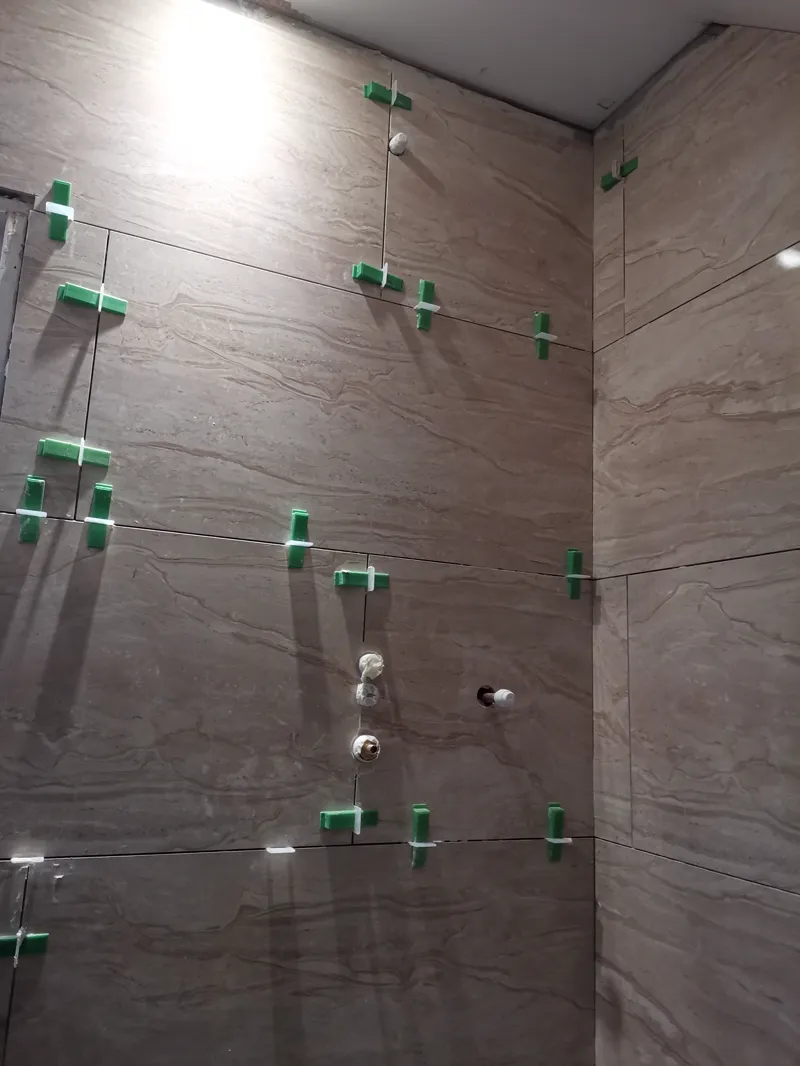 Tiled shower corner with plumbing fixtures roughed in, spacers still in place.