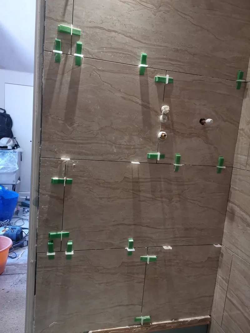 Tiled bathroom corner with plumbing fixtures roughed in, grouting not yet complete.