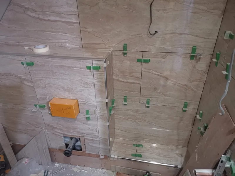 Tiled bathroom wall with an orange junction box mounted low down, tile spacers still in place.