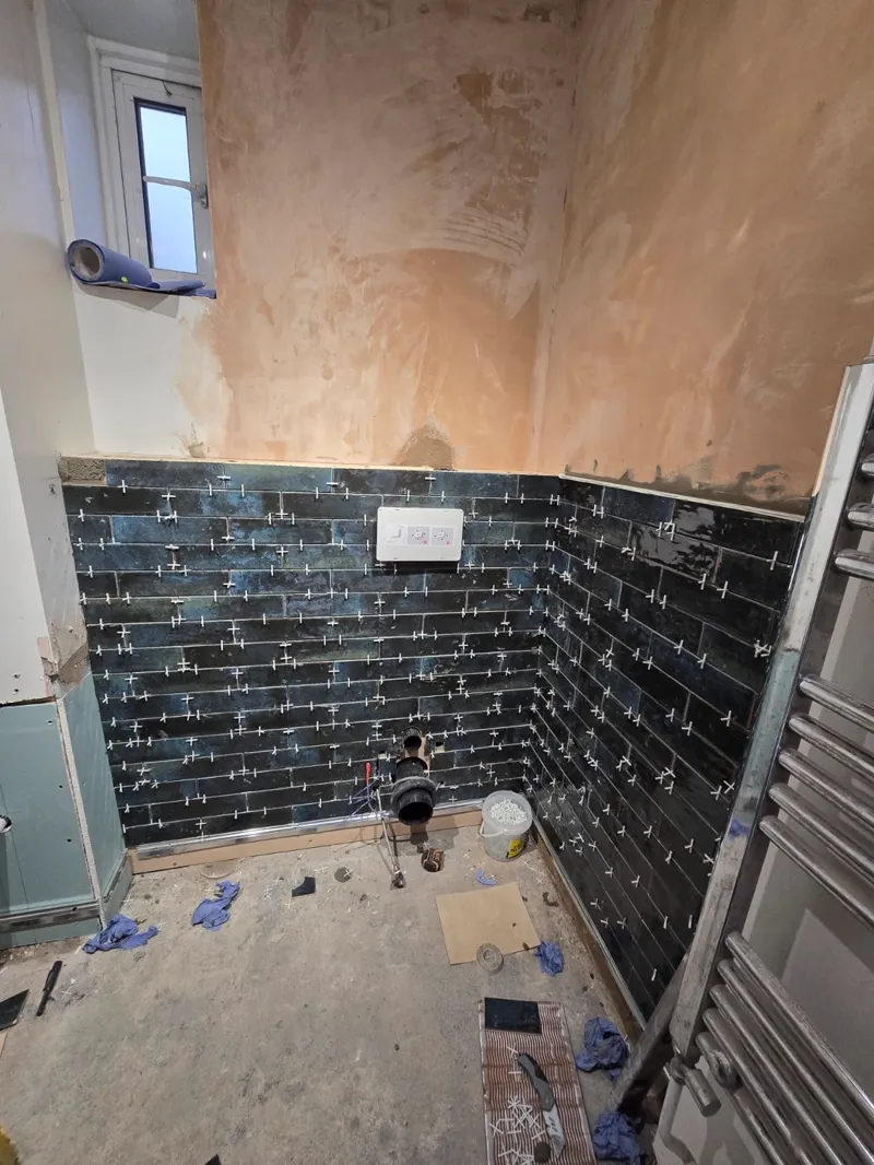 A tradesperson crouched tiling a bathroom wall and floor junction.