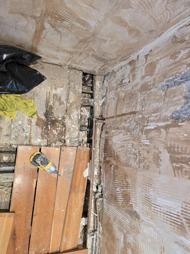 A freshly plastered wall corner with timber offcuts and a spirit level on the floor.
