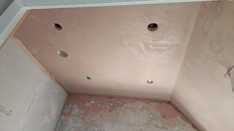 A ceiling with two downlight holes cut, freshly plastered pink base coat visible.