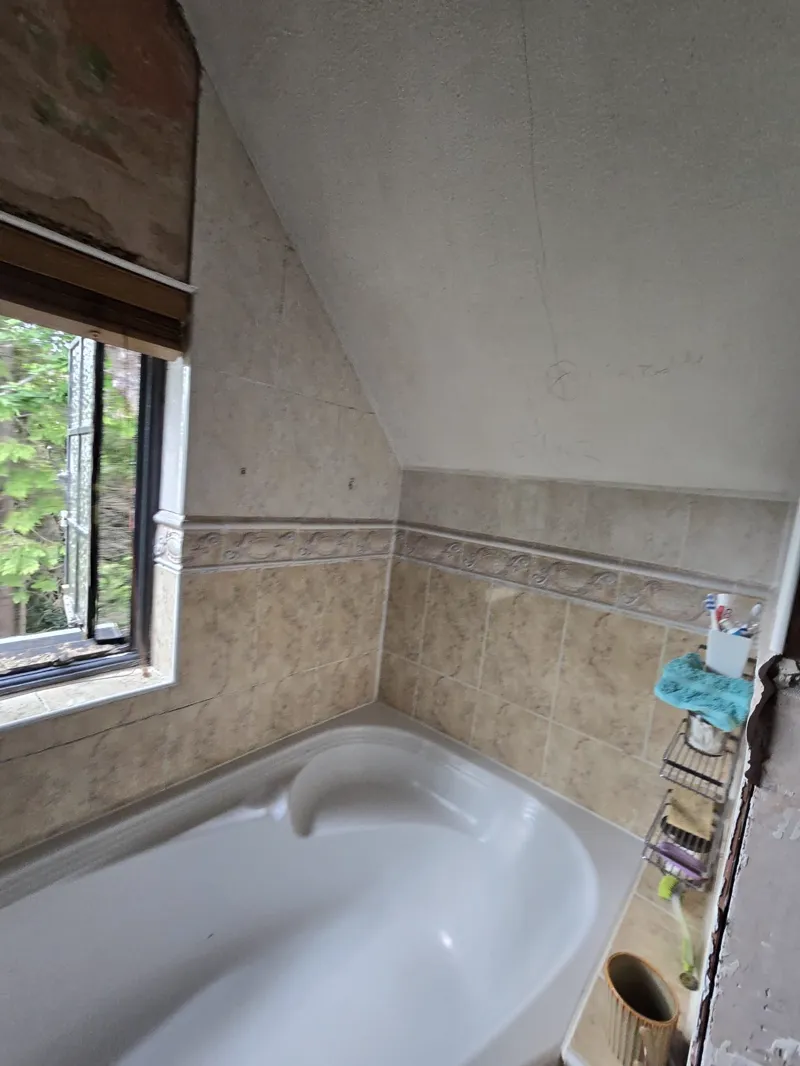 A bathtub with a beige tiled surround and a toiletry caddy, window with trees visible outside.