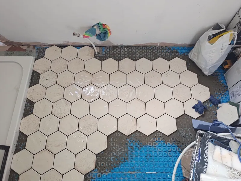 Hexagonal floor tiles being laid over underfloor-heating matting, spacers in place.