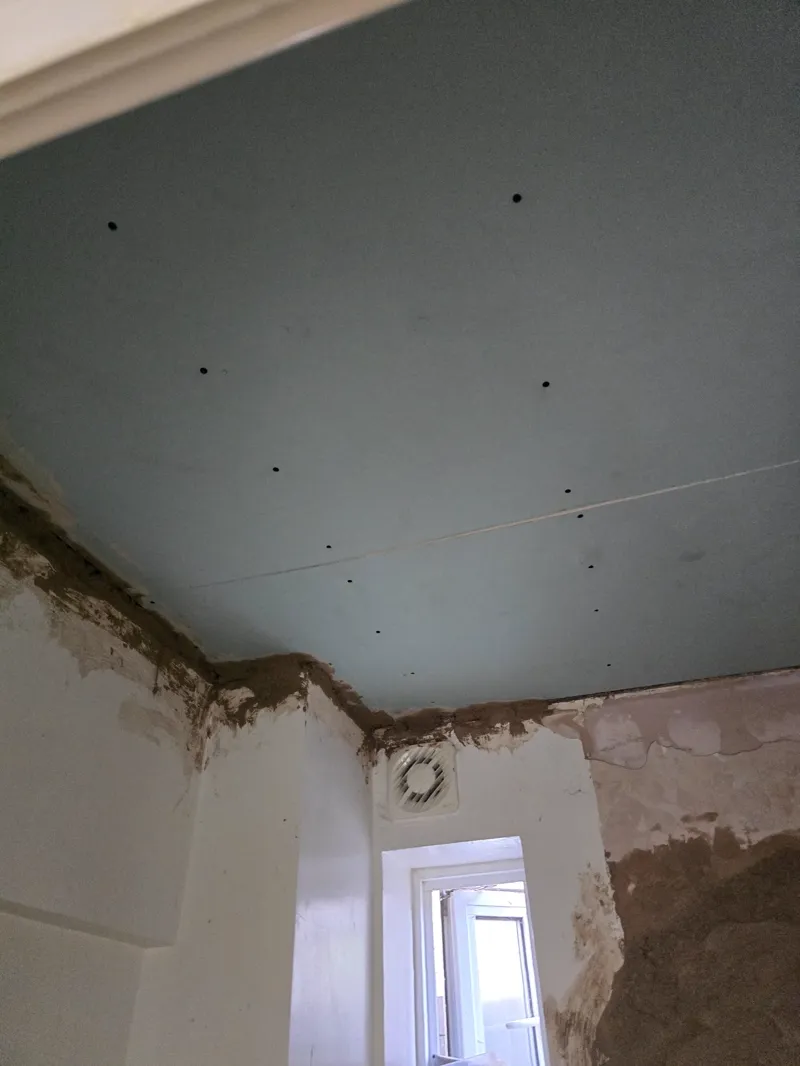 Freshly plasterboarded ceiling with a damp-stained wall corner below, doorway visible.