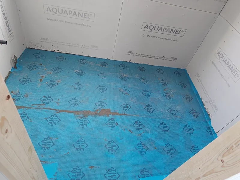Cement backer board installed on bathroom walls and floor, blue waterproofing membrane laid over the floor.