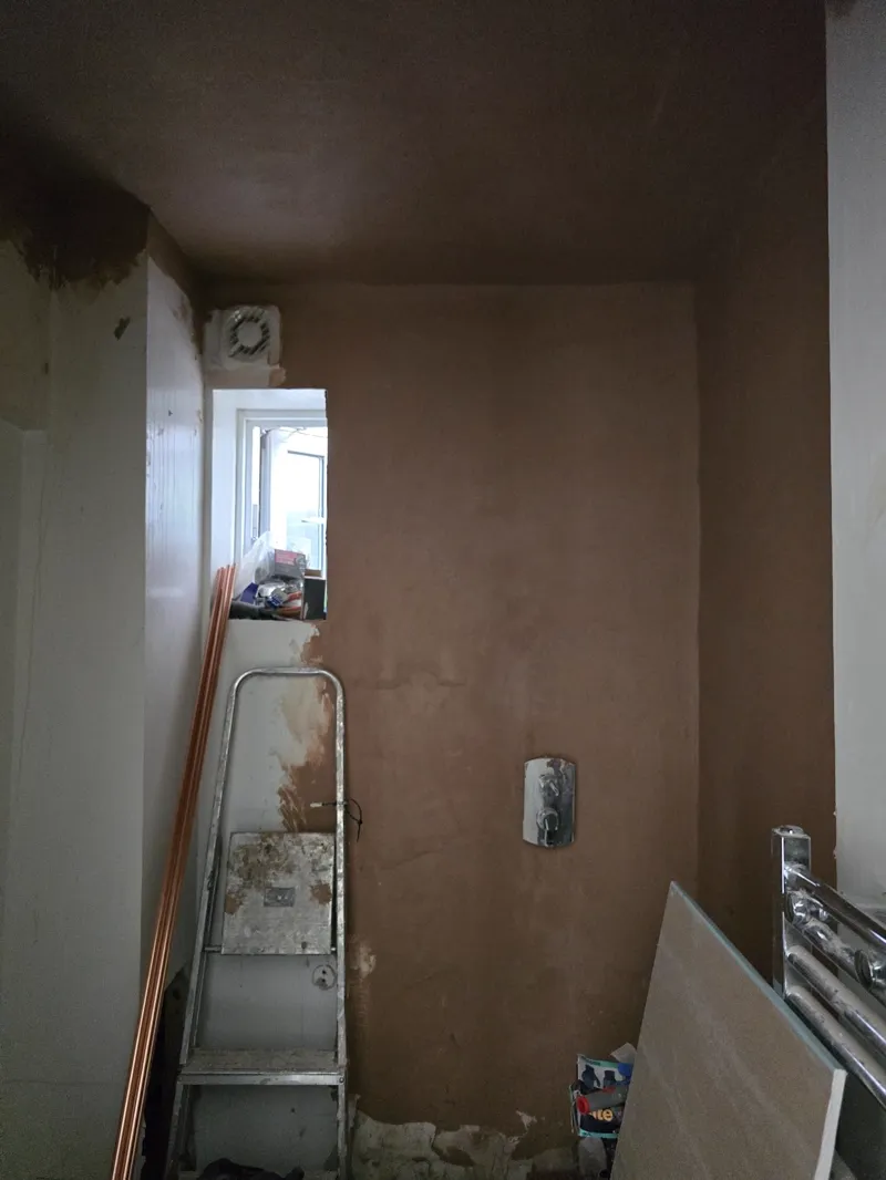 A freshly plastered bathroom wall corner with an extractor fan and a stepladder in place.